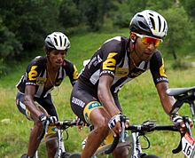 Two dark-skinned men riding bicycles.