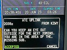 Digital display showing the aircraft registration, the date, the time in UTC "20:38:43z", and the text 'Can you keep an eye out outside for the next 20mins, you are in the area of the missing sub.'