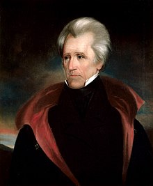 A thin man with gray hair and a tall black collar and block overcoat. The inside of the overcoat is red.
