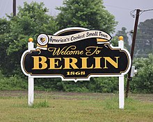 A black, white, and yellow sign that reads "America's Coolest Small Town: Welcome to Berlin 1868"