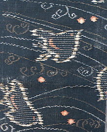 A piece of kasuri with a woven design of plovers and stylised waves on a dark indigo blue-green background. The waves are woven in both white and brown, and the plovers are woven in a mixture of white, brown and pink.