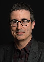 Headshot of comedian John Oliver, wearing a suit and glasses