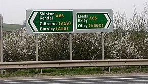 Pair of green trunk road signs, pointing left to Skipton and Kendal and right to Leeds and Otley on the A65, with other destinations indicated on other roads