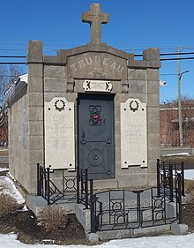 Building constructed of grey granite blocks, adorned with a cross above a metal door, and with plaques with names inscribed