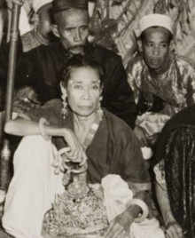 A black-and-white picture of a woman holding a crown, with two other people in the background