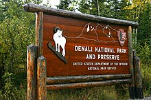 Wooden rectangular sign saying "Denali National Park and Preserve" with pictures of a mountain goat and a mountain
