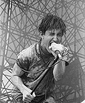 A man caked in mud screaming into a microphone.