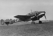 A black-and-white photograph of a twin-engine fighter aircraft standing on a grass field, shown in profile.
