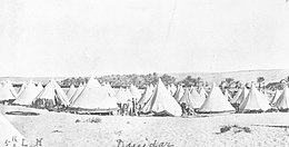 a large group of light-coloured cone-shaped tents in a desert setting