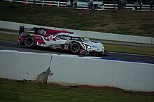 A white and pink Cadillac prototype sponsored by Ally Bank with the number 48, displayed in the 5th position, races near sunset at Road Atlanta.