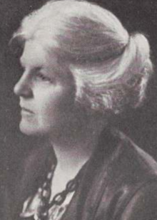 An older white woman, with white hair dressed back into a chignon, in a yearbook portrait