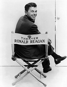 Reagan turning his head back, smiling while sitting on a director's chair that has his name on it