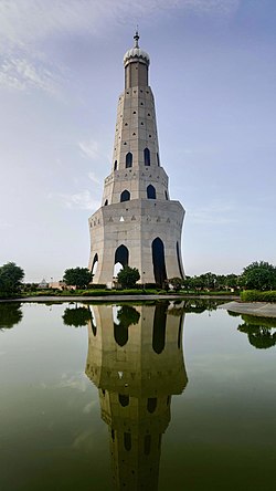 A white tower built in three step-like levels, with an onion dome on top. The tower is behind a reflecting pool, so the image shows the tower's reflection in the water.