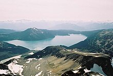 A cone-shaped mountain rising above an alpine lake in the foreground