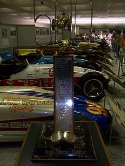 The Stark and Wetzel Rookie of the Year Award Trophy on display in front of open wheel racing cars in the Indianapolis Motor Speedway Hall of Fame Museum