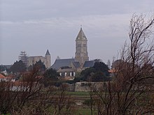 Colour photograph showing a vacant lot in the Banzeau district, with the towers of the Saint-Philbert church and the Noirmoutier castle on the horizon.