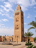 A minaret in brick with detailed decorations, some palm trees around