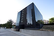 A black glass cubic building with a sidewalk and low retaining wall with "Exelon Pavilions" on it in front.