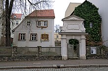 Photograph of a slightly crooked 18th century two-story house next to a stone archway