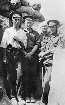 a black and white photograph of a group of males in uniform below a sandbag parapet