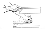 The workpiece is held against the fence of a bench hook.