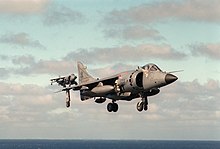 Grey jet aircraft with black radome and large engine inlet hovering with undercarriage extended. It is obscuring another identical jet in the distance. Near the bottom of the photograph, taken out at sea, is the horizon