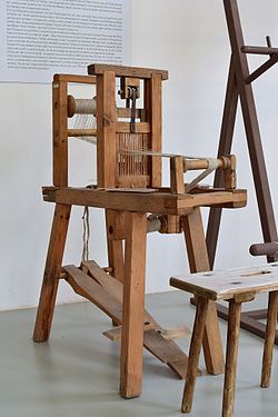 An inkle loom with a single rigid heddle, moved by treadles and a pulley; a second heddle could easily be added.