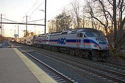 A MARC Penn Line train pulls out of Odenton station while a Northeast Regional train pulled by an AEM-7 passes through