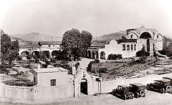 This 1921 view of the Mission San Juan Capistrano complex documents the restoration work that was already well underway by that time. The perimeter garden wall (including the ornate entranceway) and adjacent outbuilding are 1917 additions.
