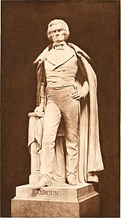 Life-sized statue, standing with full cloak to ankles, left hand on hip, right hand on book, serious and distinguished demeanor