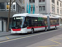 Ein Gelenktrolleybus an einer Haltestelle vor einem Geschäftshaus