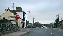 A picture of the Main Street in Newbliss, featuring the junction between the R183 and R189. Road signs for Monaghan, Three Mile House, and Aghabog are visible along with a stop sign.