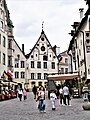 Farbfotografie eines Marktplatzes mit Pflastersteinen, der von alten Häusern umgeben ist. Das hintere Gebäude hat ein verziertes Giebelfeld.