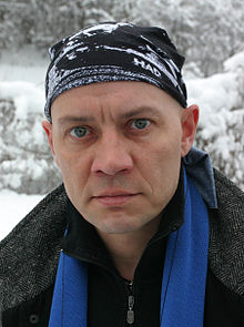 A headshot of Jaanus Raidal standing in the snow, he is wearing a "HAD" branded hat and a black coat with a blue scarf
