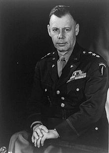 Three-quarter length portrait of seated man in uniform. He is bare-headed and wearing his medal ribbons. He is wearing the SHAEF shoulder sleeve insignia.