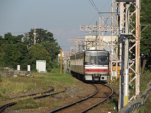 An image of a Meitetsu 5000 series passing Meiden Chikkō freight yard.