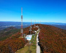 An aerial view of broadcasting towers on a forested mountain peak