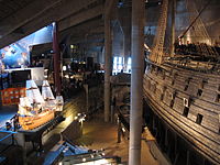 The main hall of the museum with a model of Vasa, complete with sails, to the left and the ship itself, which has no sails anymore, to the right.