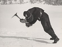 a man in polar gear leans into the face of high winds while attempting to swing an ice axe