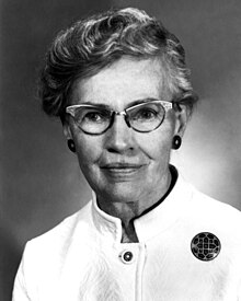 A white woman with short greying hair, wearing glasses