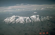 An elongated snow-covered ridge rises from a dark landscape with valleys.