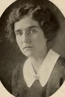 A yearbook photograph of a young white woman with short curly hair, wearing a dark garment with a white collar