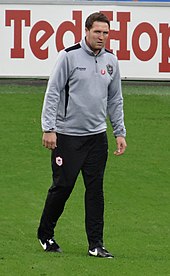 A footballer wearing a grey and black tracksuit.