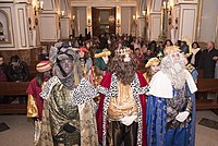 Three men disguised as kings followed by a retinue in a hall.