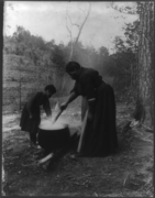 African American woman and child outdoors, standing by boiling cauldron of water, c. 1901.