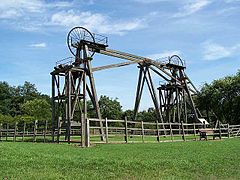 Twin timber frames of winding gear topped with spoked metal wheels used to hoist men and coal from underground on a sunny day