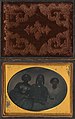 Formal portrait of three African American women in formal dress with hands clasped together, tinted and with gilded jewelry, studio-ferrotype in typical casing, c. 1856