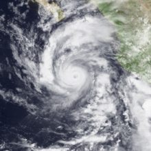 A satellite image of a hurricane whose cloud pattern resembles the number 6, with a cloudy eye in the middle; some streaky but deep clouds in the lower right are those of a nearby tropical storm