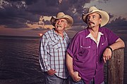 Country music duo The Bellamy Brothers, standing in front of a purple sunset-themed backdrop.