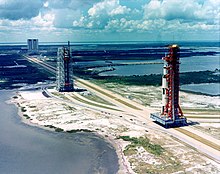 A tall rocket on a platform is rolled out along a track towards a launch site